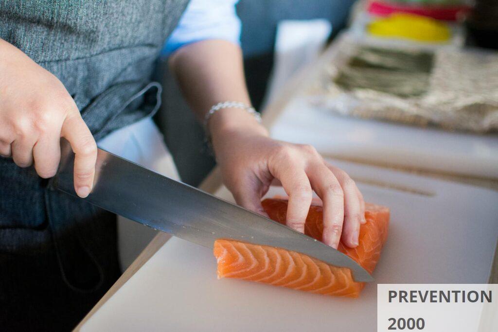Close-up of a chef's hands slicing fresh salmon for sushi on a cutting board indoors.